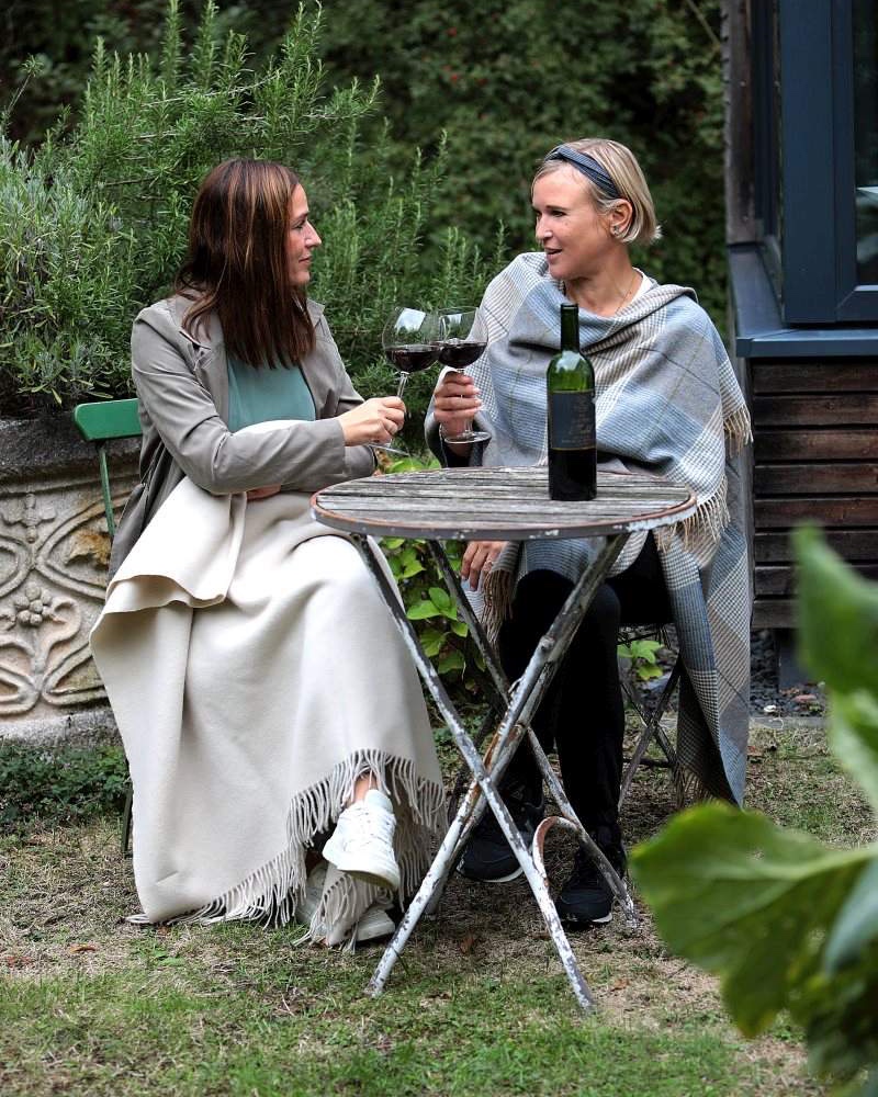Zwei Frauen mit Wolldecken und Cape am Gartentisch